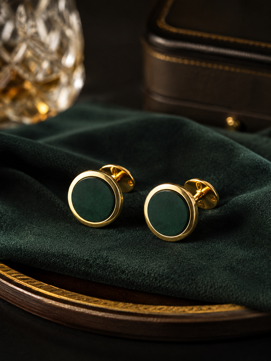 Green cufflinks with gold trim on a dark green fabric surface.
